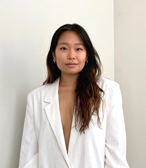 Woman in a white blazer smiling at a camera, plain white background 