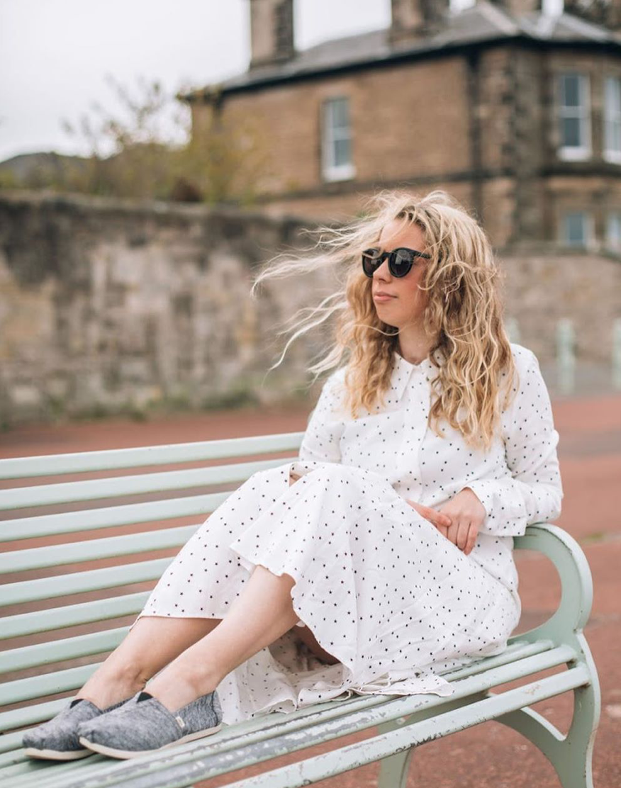 Woman wearing a white polka dot dress and sunglasses, sitting on a pastel green bench