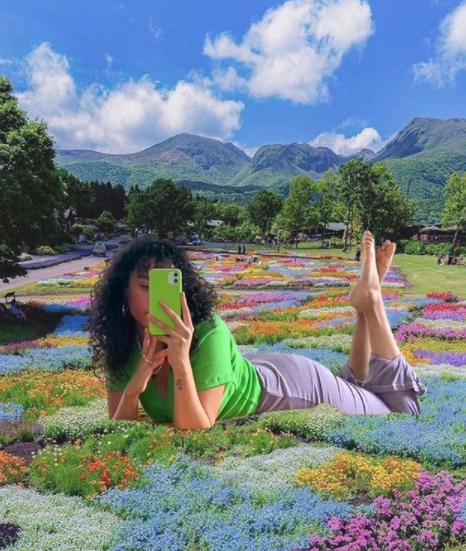 Woman lying in a multicoloured field of flowers, trees and mountains in the background