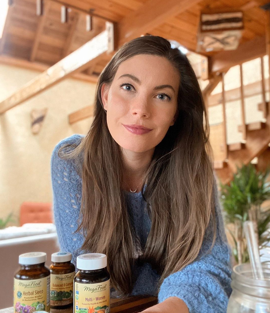 Woman smiling next to 3 bottles of multi-vitamins