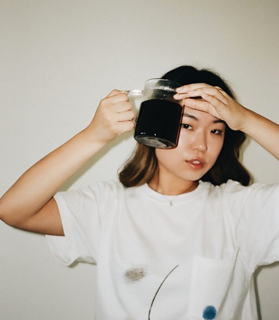 Woman in a white t-shirt holding a clear mug full of a dark liquid above her head