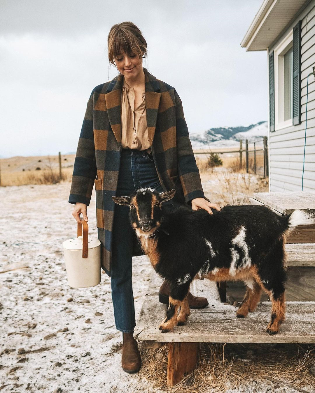 Woman standing in her garden, in front of her is a black and brown goat