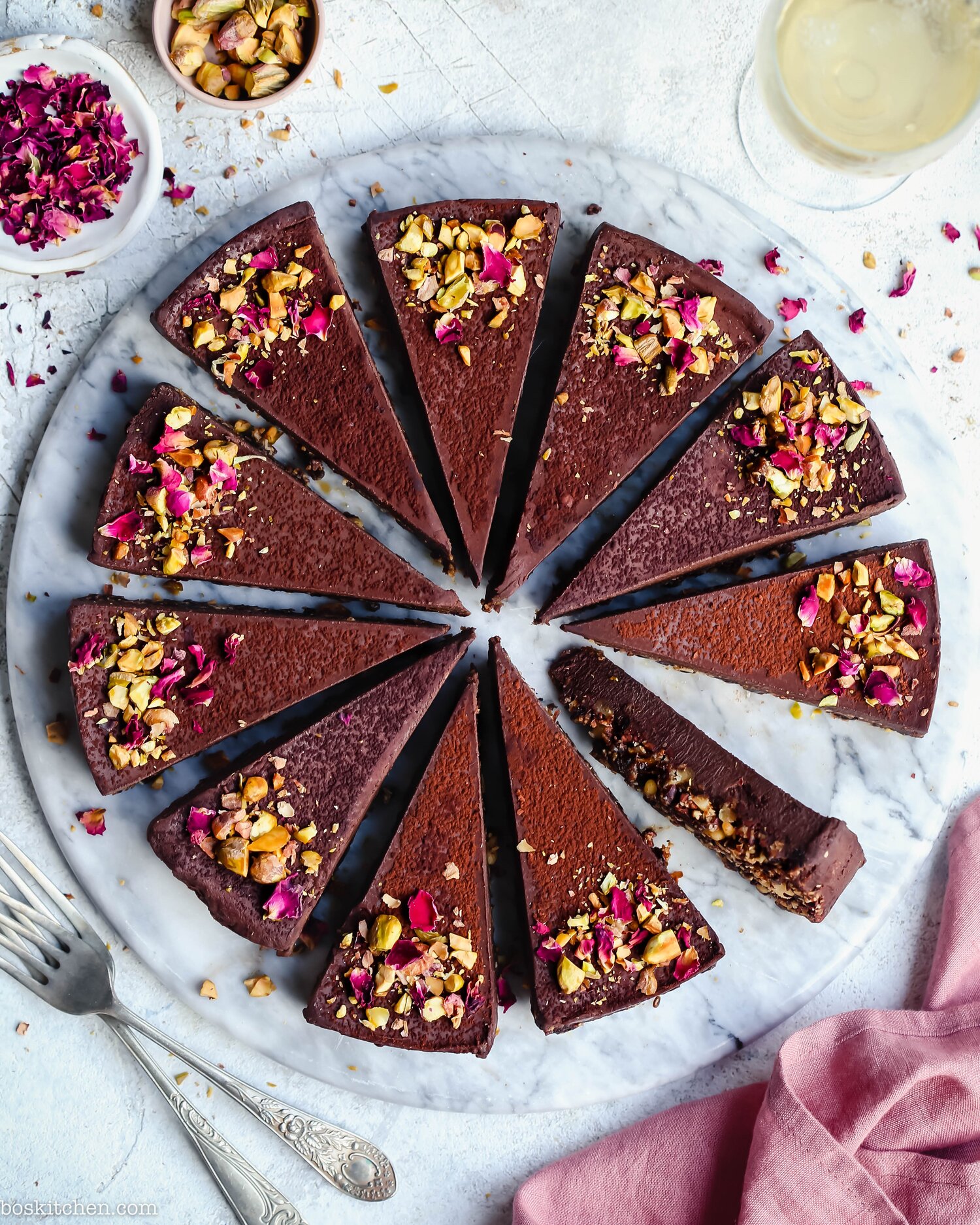 A chocolate cake cut up into equal sections, decorated with pink and white petals, one slice is lying on its side