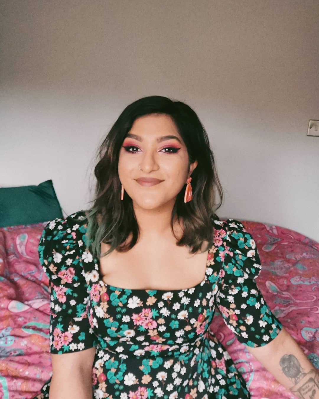 Woman sitting on her bed in green floral dress, smiling at a camera